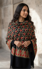 Load image into Gallery viewer, Woman wearing a patterned shawl with red and gold design against a stone wall.