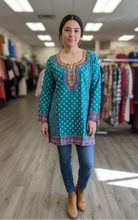 Load image into Gallery viewer, Woman wearing a teal patterned dress in a clothing store